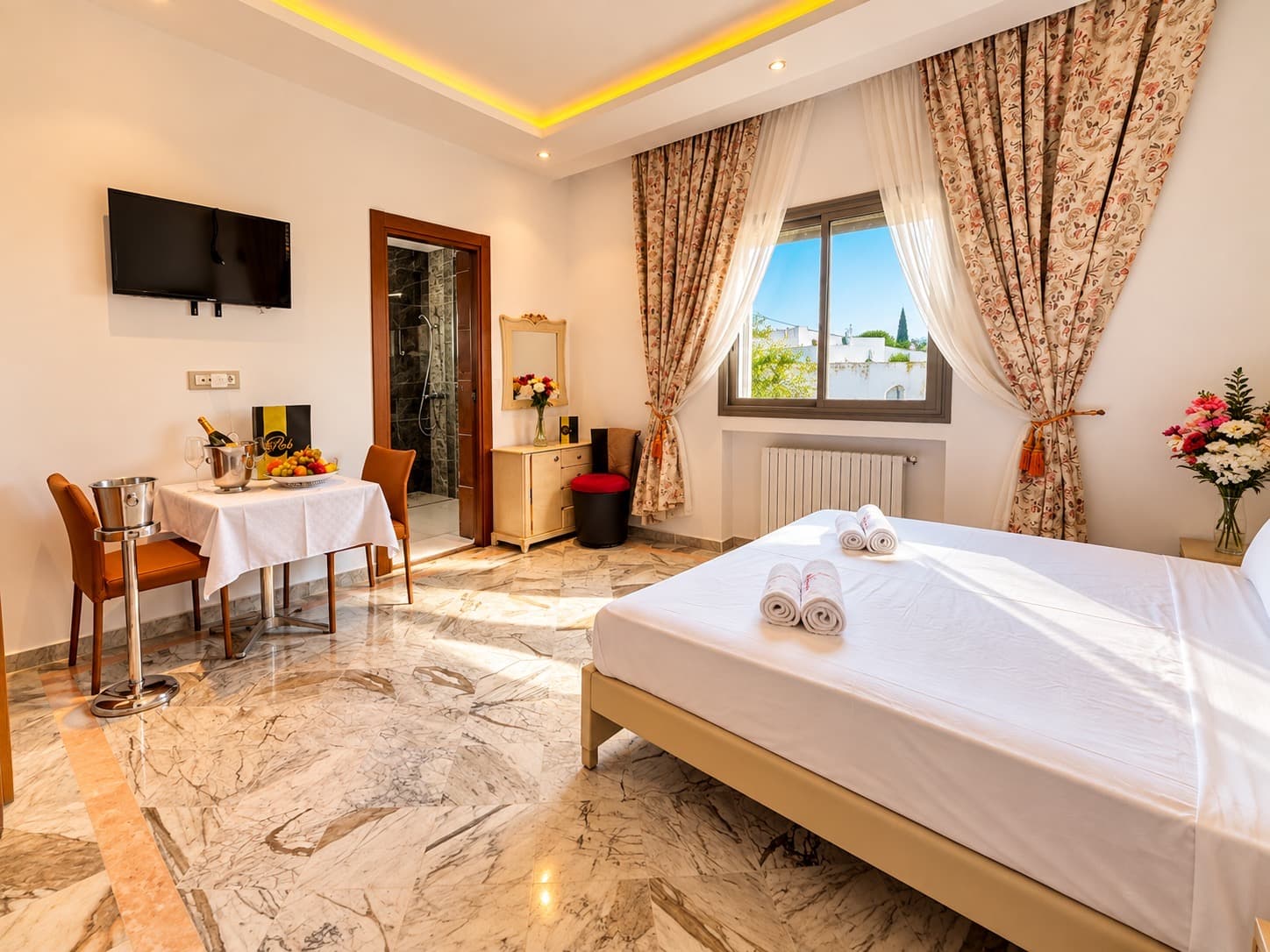 Chambre spacieuse avec rideaux fleuris, coin repas et salle de bain attenante